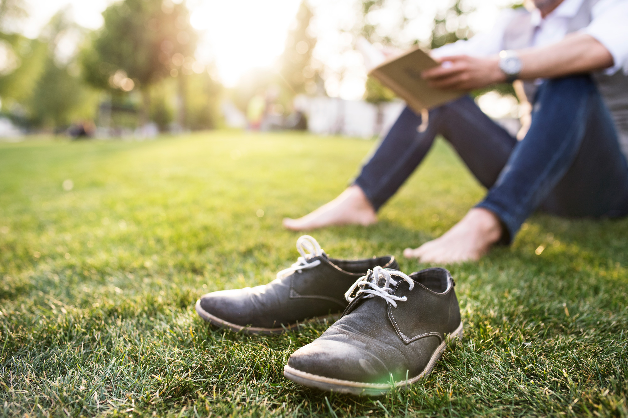 Photo of a person sitting barefoot in a park reading