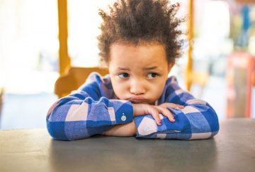 Picture of young child sitting at table looking puzzled