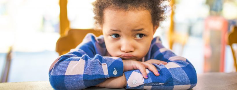 Picture of young child sitting at table looking puzzled