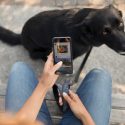 Picture of a person holding a phone with a black dog in the background