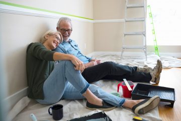An older couple sitting on the floor of a room they just painted.