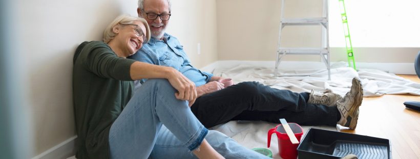 An older couple sitting on the floor of a room they just painted.