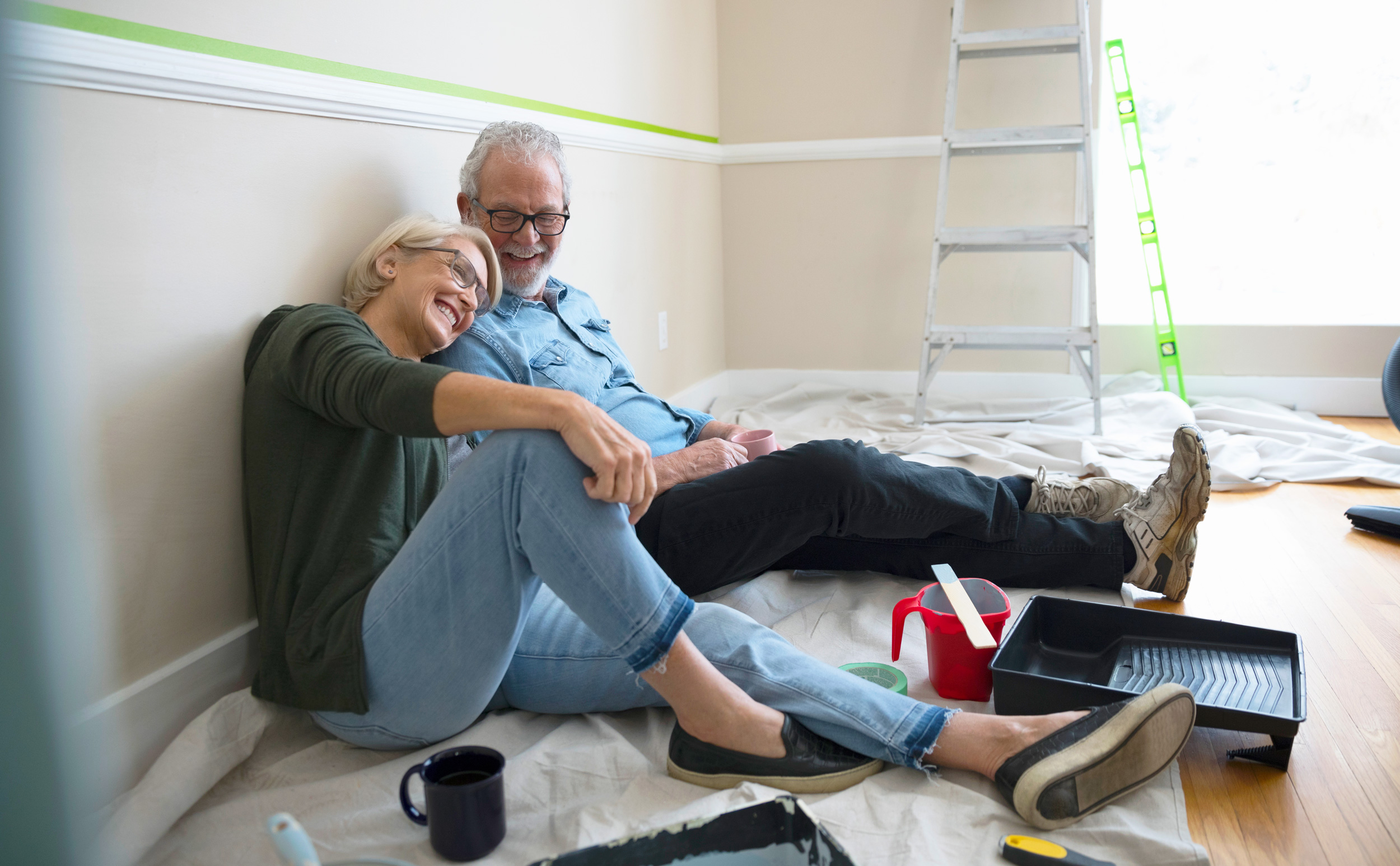 An older couple sitting on the floor of a room they just painted.