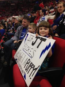 Picture of two kids holding a sign sitting in a hockey arena.