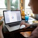 Picture of a person sitting at a kitchen table working at a laptop.