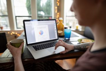 Picture of a person sitting at a kitchen table working at a laptop.