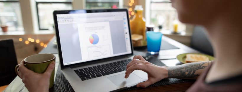 Picture of a person sitting at a kitchen table working at a laptop.